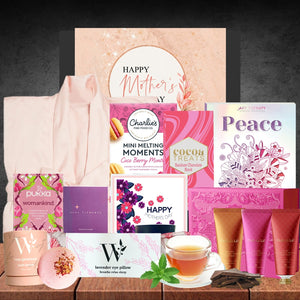 Collection of Mother's Day gifts including tea, bath bombs, and a candle on a wooden surface.