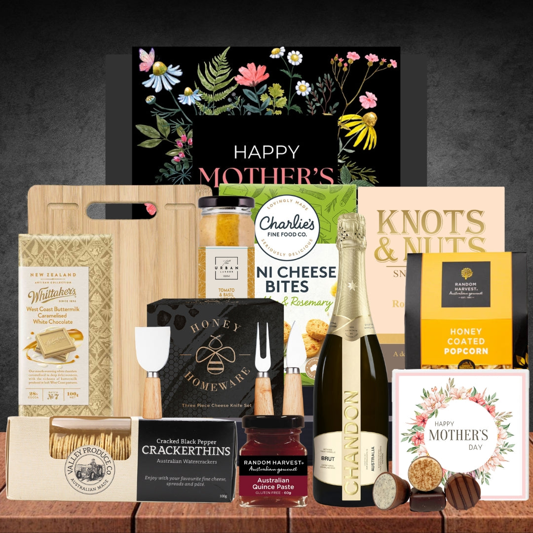 Gourmet gift basket with Mother's Day card, champagne, and assorted snacks on a wooden surface.