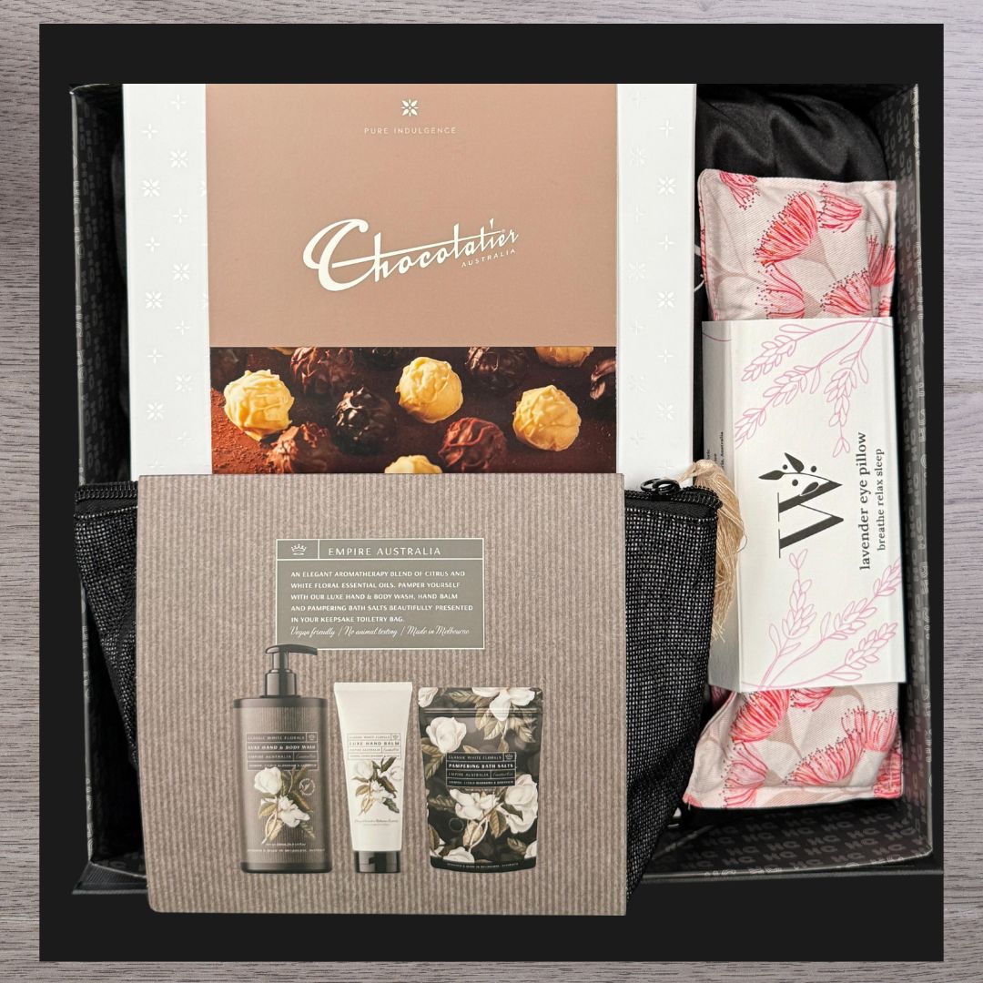 Gift box with assorted items including a Chocolatier chocolate box, Empire Australia skincare set, and a lavender eye pillow with floral design.