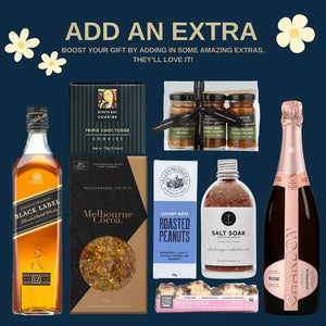 Gift assortment on a navy background features whiskey, rosé, cookies, chocolate, nuts, mustards, bath salt, and a rocky road bar, with flowers.