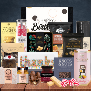 Assorted gourmet snacks and treats on a wooden surface with a 'Happy Birthday' card.