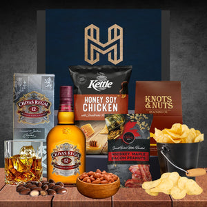 Gourmet gift set with Chivas Regal whiskey, snacks, and Kettle chips on a wooden surface.
