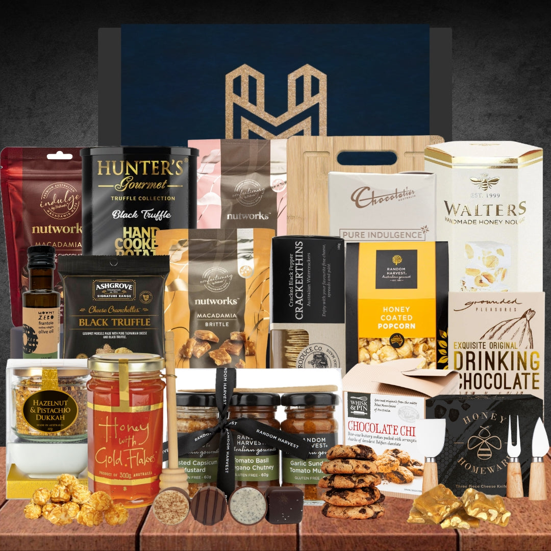 A gift hamper containing various gourmet snacks and chocolates, including items like chocolate honeycomb, nougat, macadamia nut products, and more, all packaged in a stylish gift box with a blue background and gold accents.