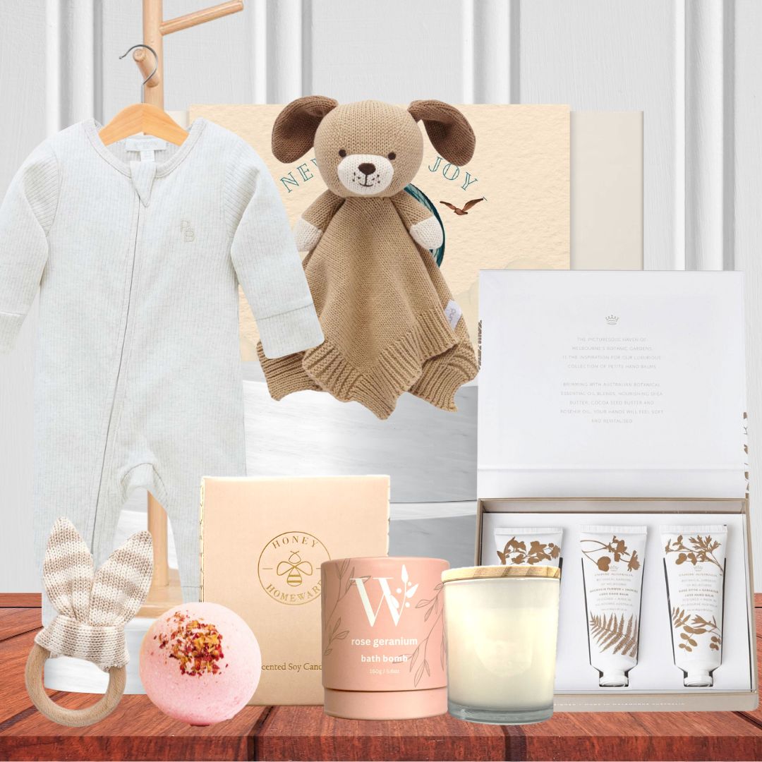 A baby hamper gift set containing a knitted dog comforter, grow suits, teethers, bath bombs, hand creams, a soy candle, and a botanical gardens luxe hand balm trio.