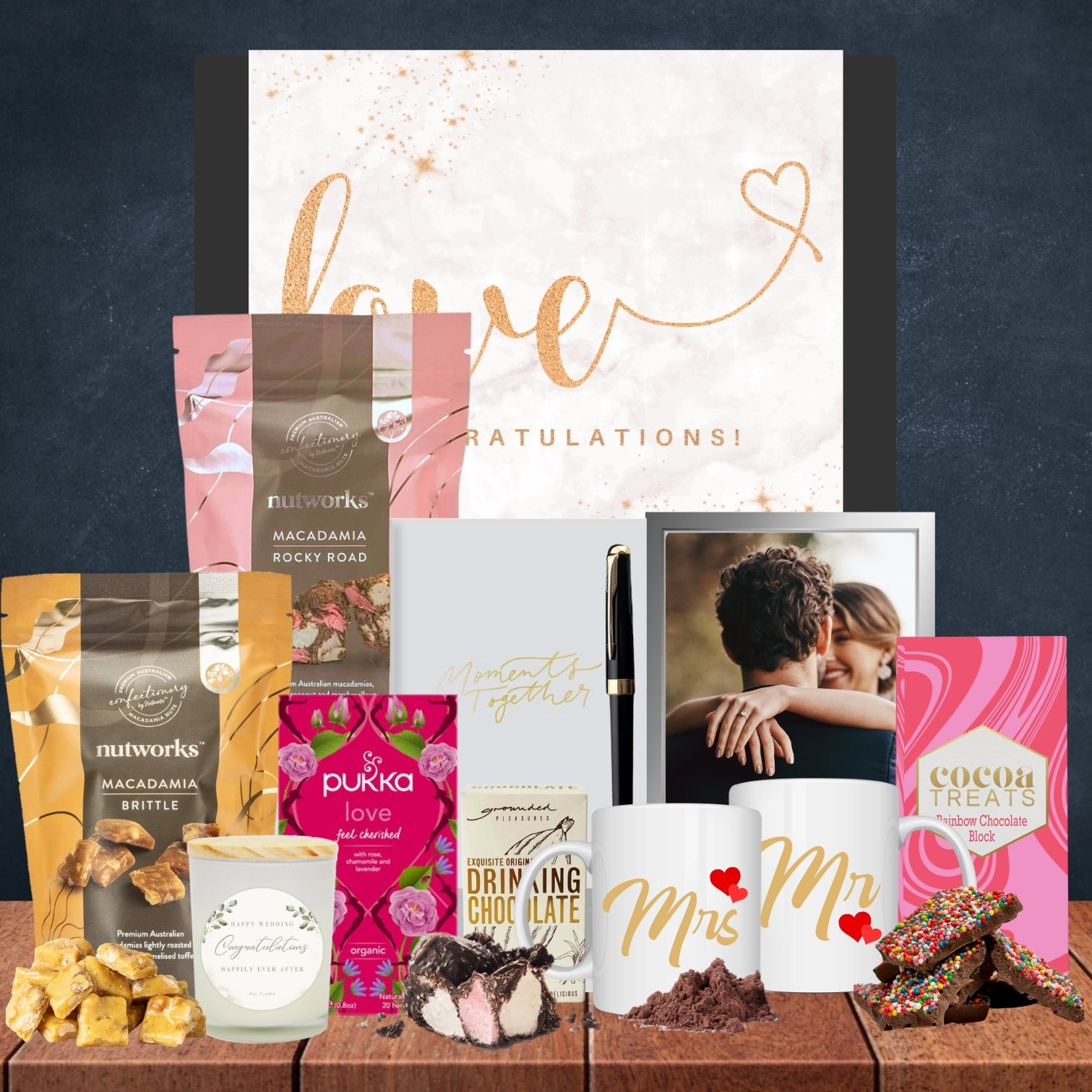 Collection of gifts including mugs, snacks, and a photo frame on a dark background