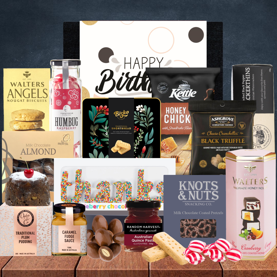 Assorted gourmet snacks and treats on a wooden surface with a 'Happy Birthday' card.