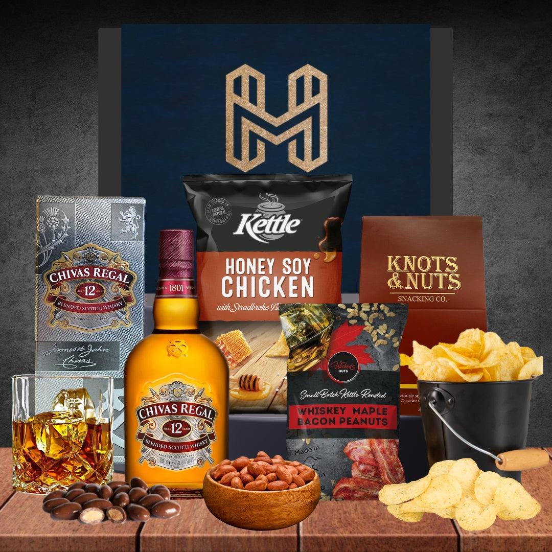 Gourmet gift set with Chivas Regal whiskey, snacks, and Kettle chips on a wooden surface.