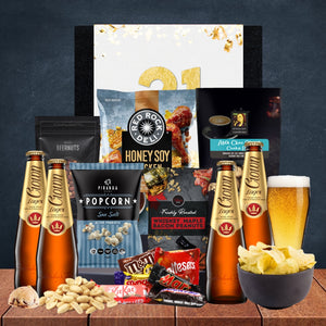 Gourmet gift basket with beer, snacks, and candies on a wooden surface.