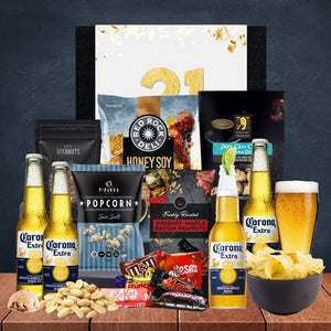 Gourmet gift set with Corona Extra beer, popcorn, and snacks on a wooden surface.