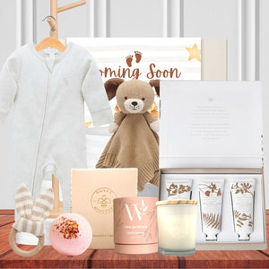 Collection of baby products including a teddy bear, baby onesie, and candles on a wooden surface.